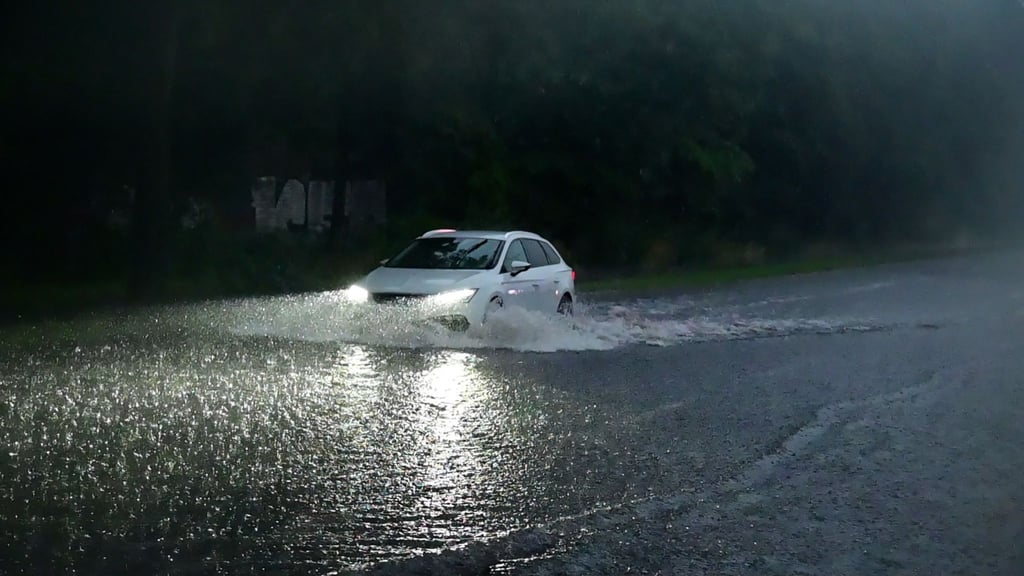 Ein Auto fährt durch eine überflutete Straße.