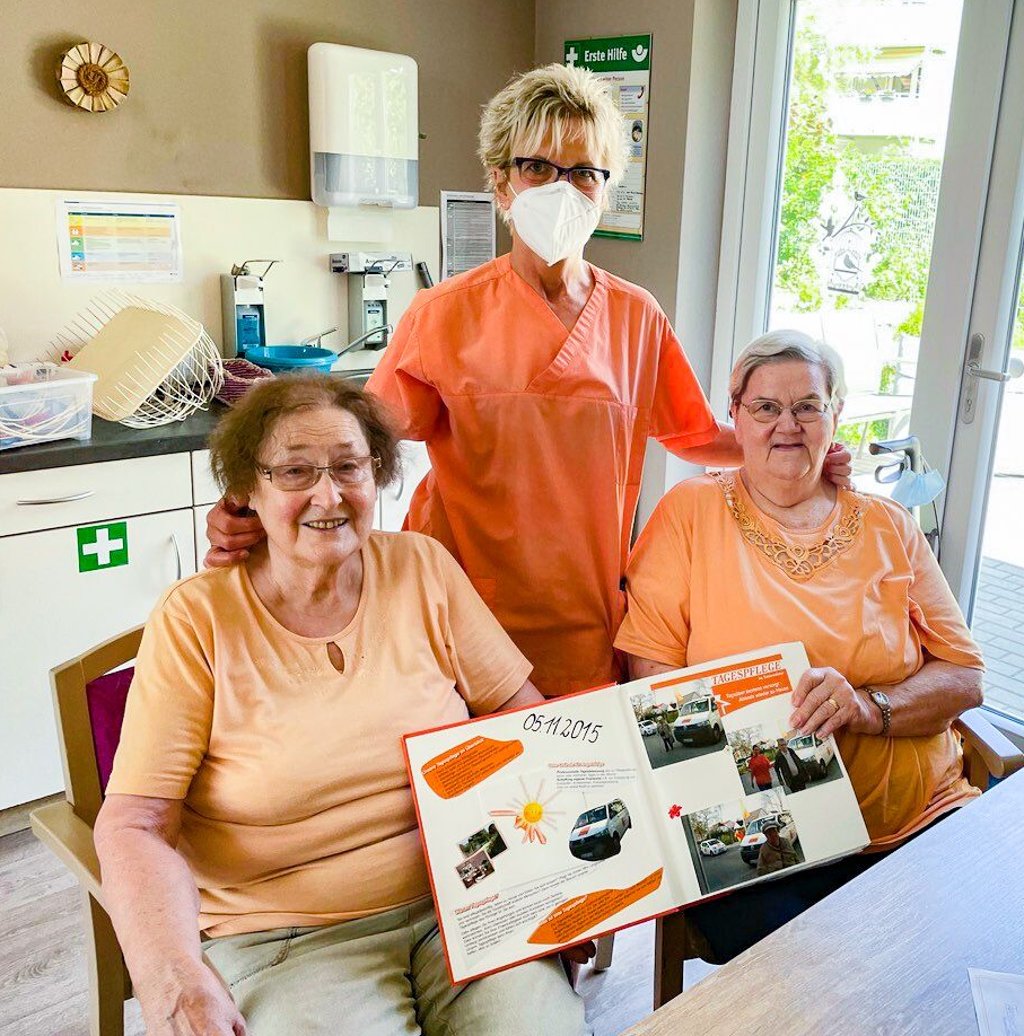 Unter den Augen von Teamleiterin Iris Wiebigke zeigen Ruth Patzer (links) und Christin Eckert (rechts) ein Fotoalbum der Tagespflege in die Kamera. In dem werden Feste und Veranstaltungen festgehalten.