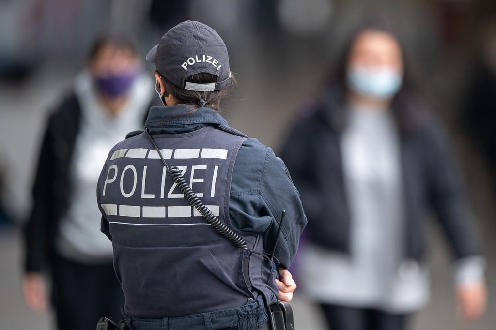 Eine Polizistin Blickt zu Passanten mit Masken.