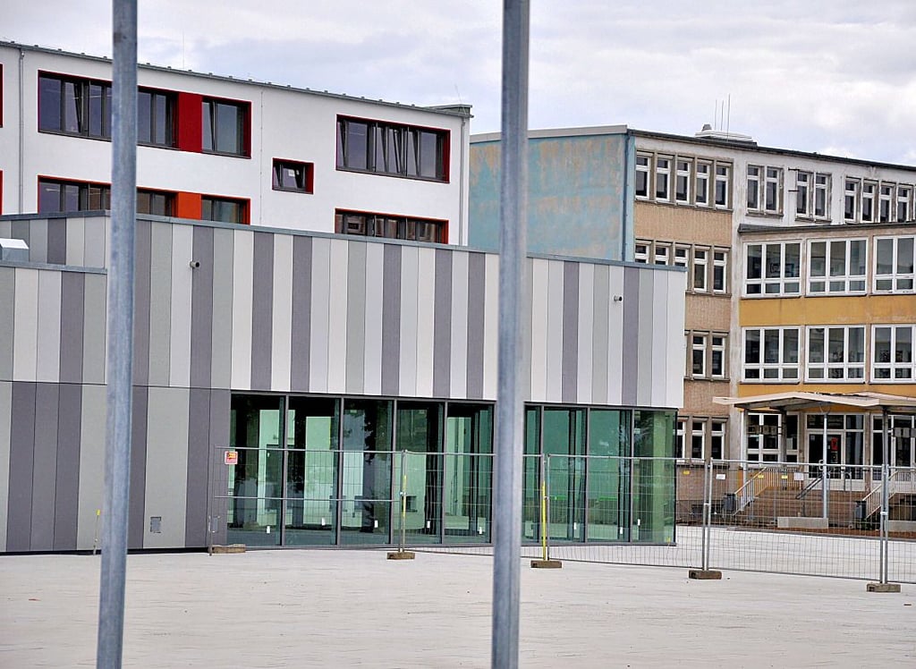 Auf der Südseite des Schulgeländes ist der Schulhof bereits gepflastert. Links im Bild sind das sanierte Gebäude und davor der Neubau zu erkennen, auf der rechten Seite das bislang genutzte Gebäude.