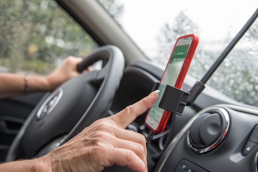 Eine Autofahrerin bedient ein Handy mit Navi.