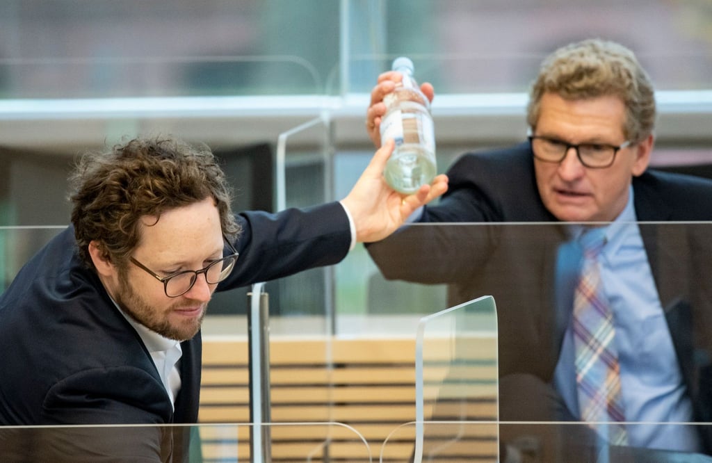 Jan Philipp Albrecht (Bündnis 90/Die Grünen, l), Minister für Energiewende, Landwirtschaft, Umwelt, Natur und Digitalisierung des Landes Schleswig-Holstein, reicht Bernd Buchholz (FDP), Minister für Wirtschaft, Verkehr, Arbeit, Technologie und Tourismus des Landes Schleswig-Holstein im Plenarsaal des Landtags eine Flasche Wasser.