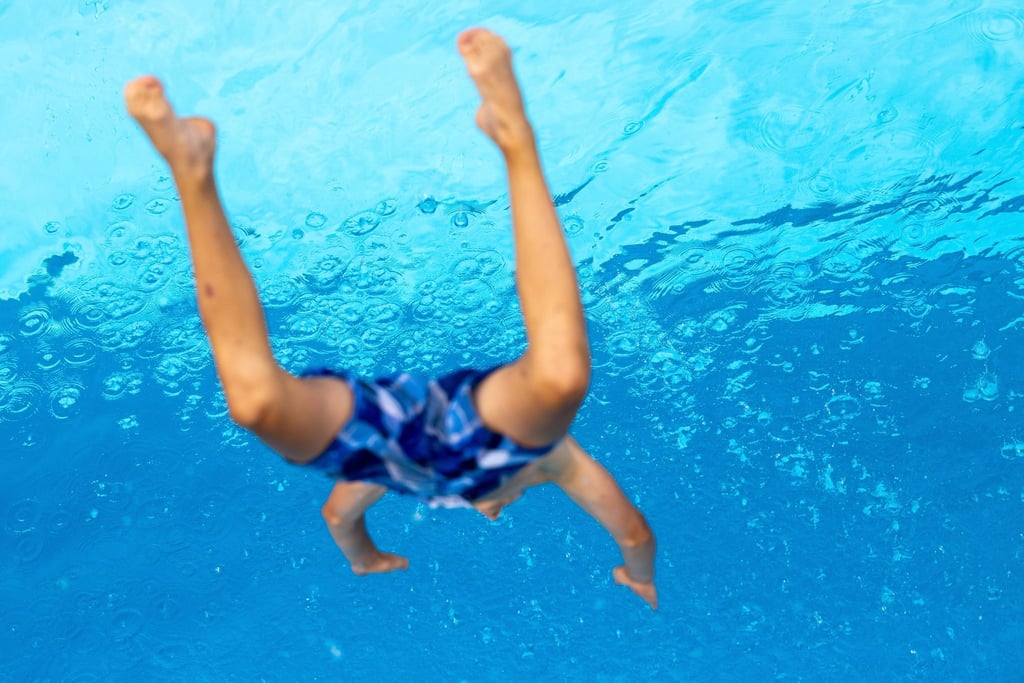 Ein Kind springt im Freibad ins Wasser.
