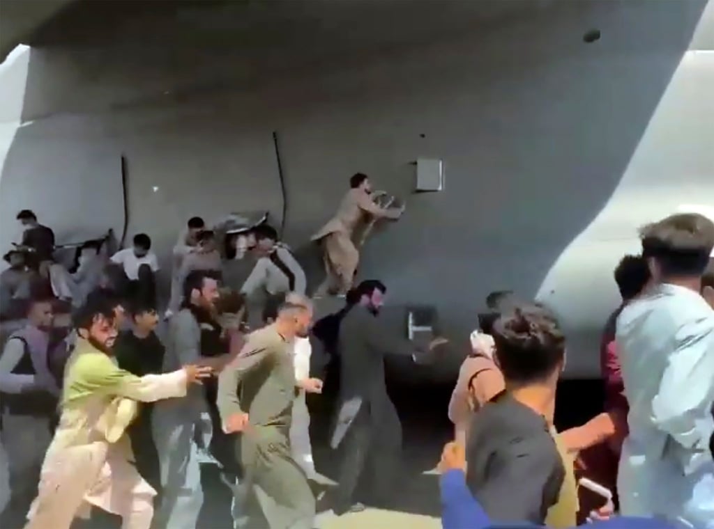 Menschen laufen auf dem Rollfeld des Flughafens Kabul neben einer Boeing C-17 der United States Air Force und versuchen, sich an die Maschine zu klammern.
