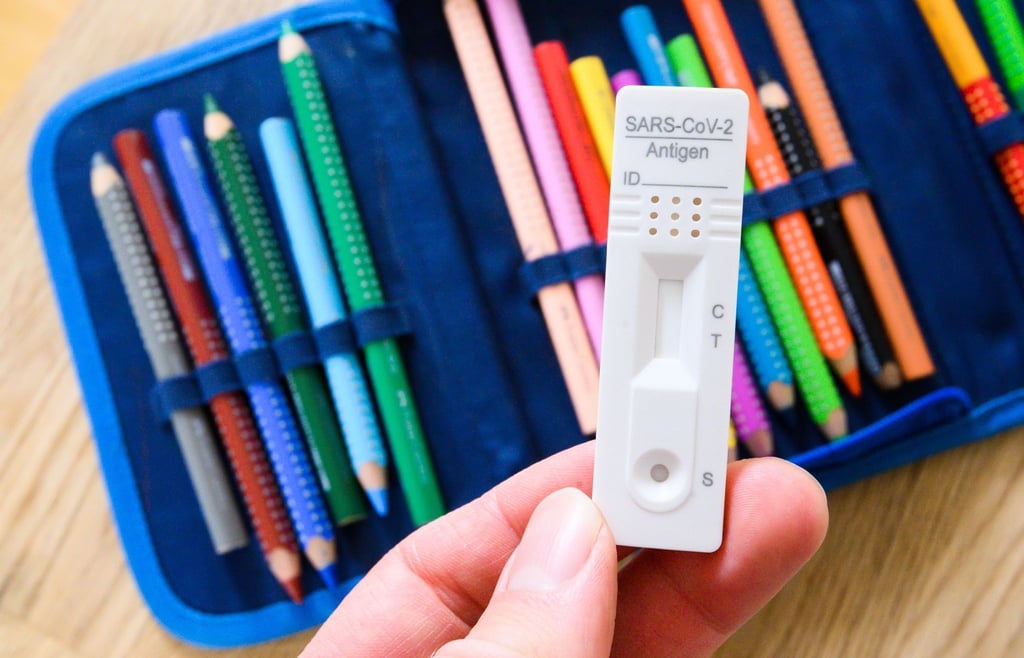 Ein Corona-Selbsttest wird über dem Federmäppchen eines Grundschülers gehalten.