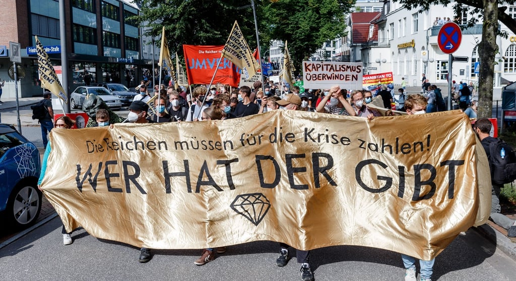 Demonstranten mit Transparent mit Aufschrift "Die Reichen müssen für die Krise zahlen! Wer hat, der gibt".