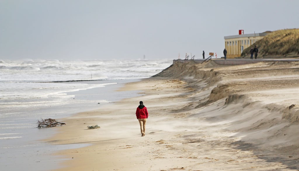 Ein Mann spaziert über den Strand unterhalb der Abbruchkante der letzten Sturmflut.