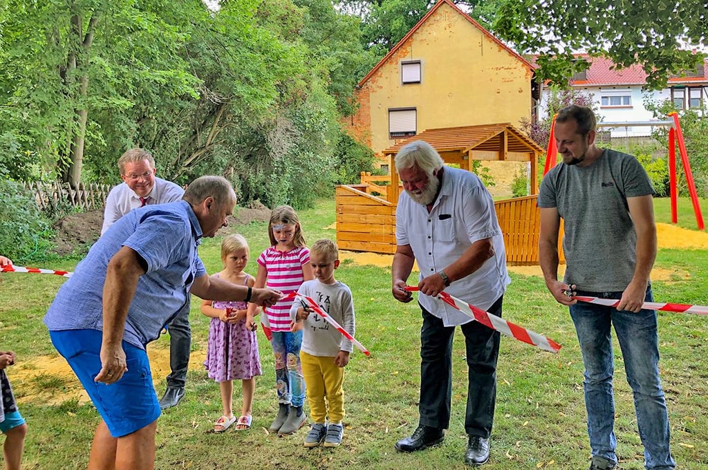 Gemeinsam mit Kindern geben Thales Bürgermeister Maik Zedschack (l.), Ortsbürgermeister Dirk-Michael Meisel (M.) und Ortschaftsratsmitglied Matthias Hohley (r.) den neuen Spielplatz frei.