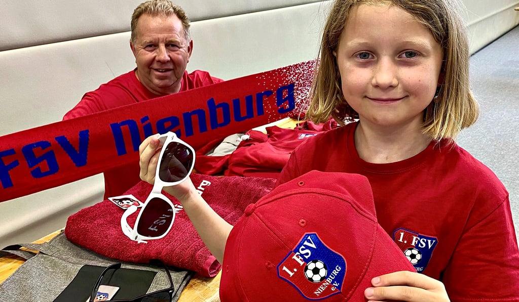 Mario Thiele präsentiert mit seiner Enkelin Jil die Fanartikel des 1. FSV Nienburg.