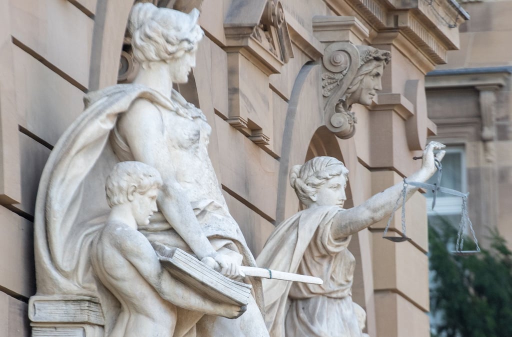 Vor einem Gerichtsgebäude steht u.a. eine Statue der Justitia.