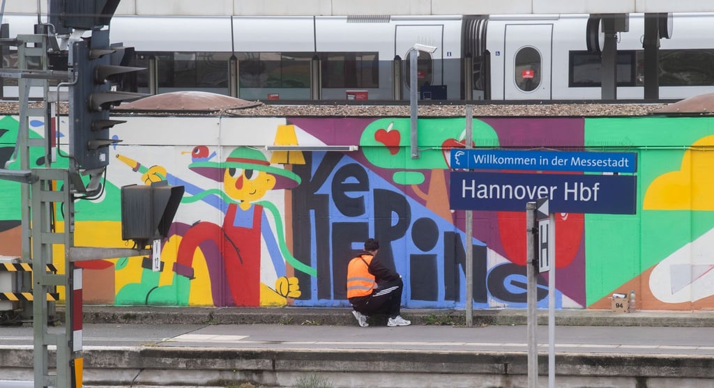 Das Künstlerkollektiv DOTU sprayt ein großes Kunstwerk auf ein Gebäude der Deutschen Bahn auf Gleis 9 und 10 des Hauptbahnhofes in Hannover.