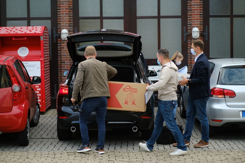 Zivilpolizisten tragen vor dem DRK-Gebäude Kartons in ein Zivilfahrzeug der Polizei.