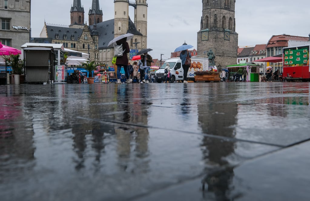 Menschen laufen bei Regen durch die Altstadt von Halle.