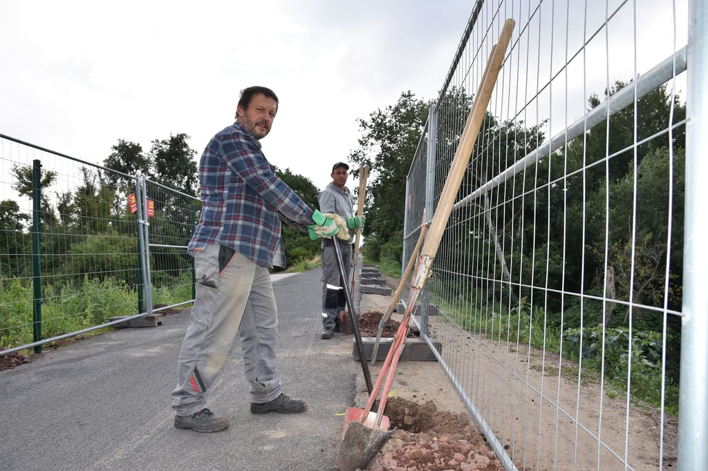 Mitarbeiter der Magdeburger Latowo GmbH installieren einen festen Zaun am Radweg.