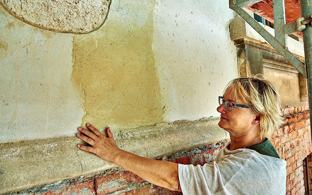 Hochbau-Dezernentin Silvia Ristow zeigt eine Stelle an der Fassade, an der neben dem alten groben Putz (oben) mit neuen Mischungen experimentiert wurde.
