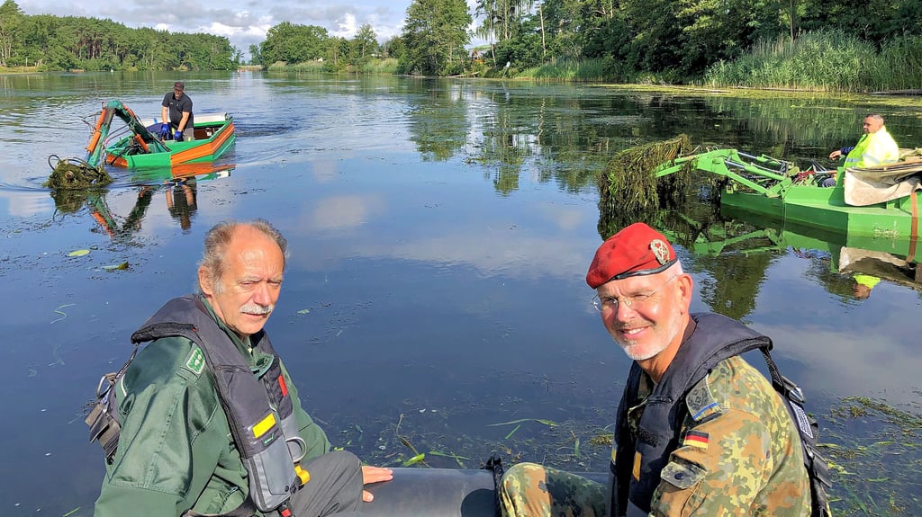 Wolfgang Rost vom Bundesforstamt und Kommandeur Oberstleutnant Roman Jähnel machen sich ein Bild vom Mähen des Klietzer Sees. Links ist das Mähboot zu sehen, rechts das Boot, das die abgeschnittenen Pflanzen einsammelt.