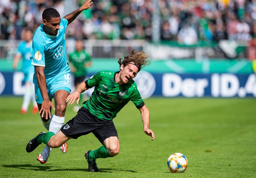 Wolfsburgs Maxence Lacroix (l) bringt Münsters Jules Schwadorf im Zweikampf zu fall.