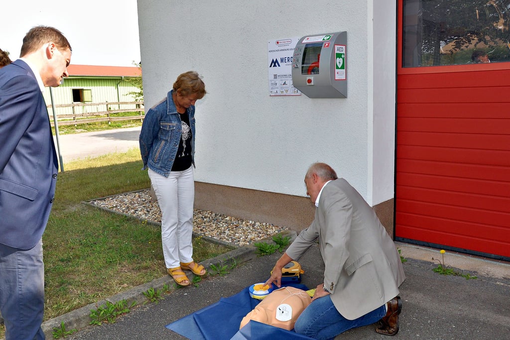 Ein Defibrillator befindet sich am Gerätehaus in Hohenberg-Krusemark. Thomas Pflanz von der Björn Steiger Stiftung zeigt Simone Kuhlmann, stellvertretende Bürgermeisterin der VG, und André Listemann, Chef von Mercer, die leichte Bedienung.