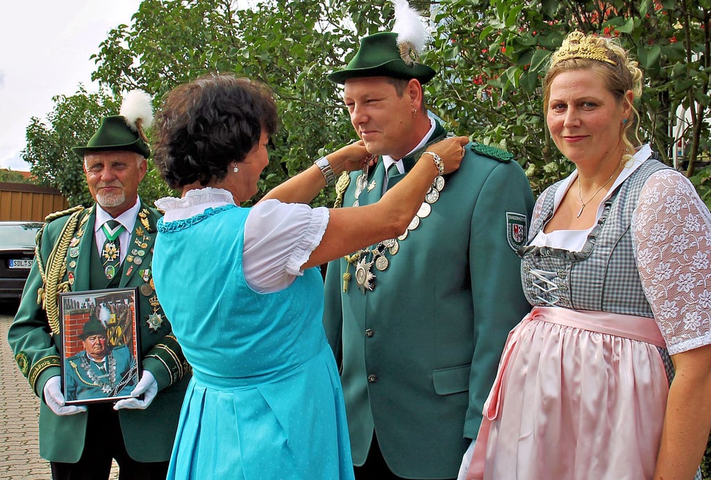 Christiane Reddigan richtet für den neuen Schützenkönig die Schützenkette. Vereinsvorsitzender Hans-Georg Schnell (links) hält das Bild des verstorbenen Vorjahres-Königs in den Händen.