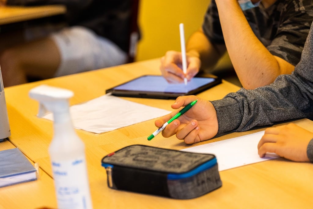 Ein Schüler hält beim Unterricht in seiner Klasse einen Stift, während ein anderer mit einem Tablet arbeitet.