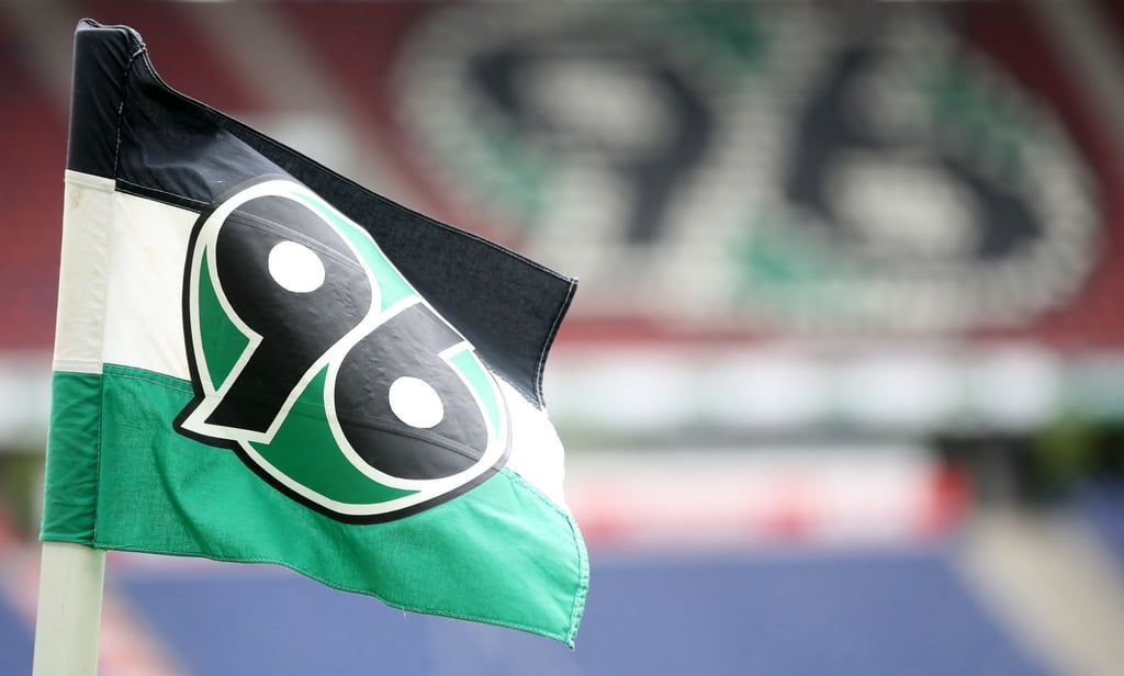 Das Logo von Hannover 96 ist vor den leeren Sitzen der Zuschauertribüne auf einer Fahne zu sehen.