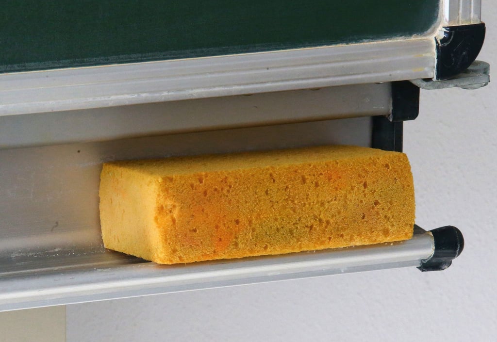 Eine Schultafel mit Tafelschwamm steht in einem Klassenzimmer.