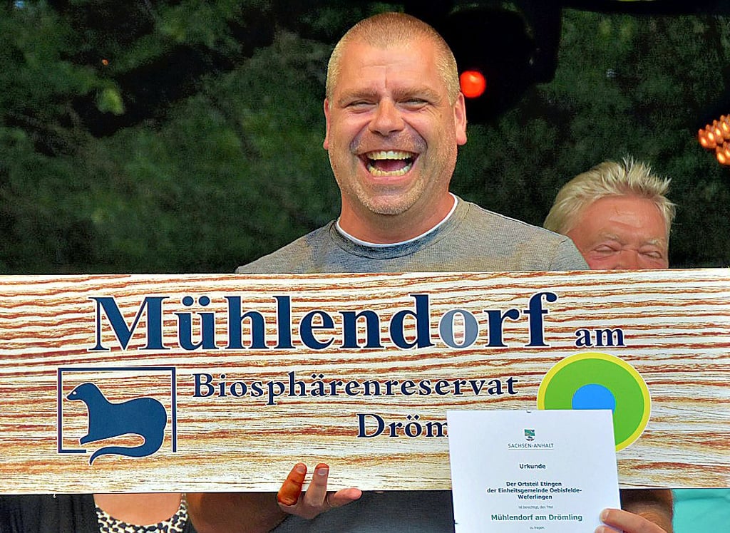 Etingens Ortsbürgermeister Marko Alex freut sich, denn sein Ort hat sich erfolgreich beim Ideenwettbewerb um den Titel ?Mühlendorf am Biosphärenreservat Drömling? beworben und darf sich nun mit dem Titel schmücken. Beim Drömlingsfest nimmt der Ortschef auf der Hauptbühne in Oebisfelde das große Schild, das demnächst am Ortseingang von Etingen befestigt werden soll, vom Biosphärenreservatsleiter Fred Braumann entgegen.
