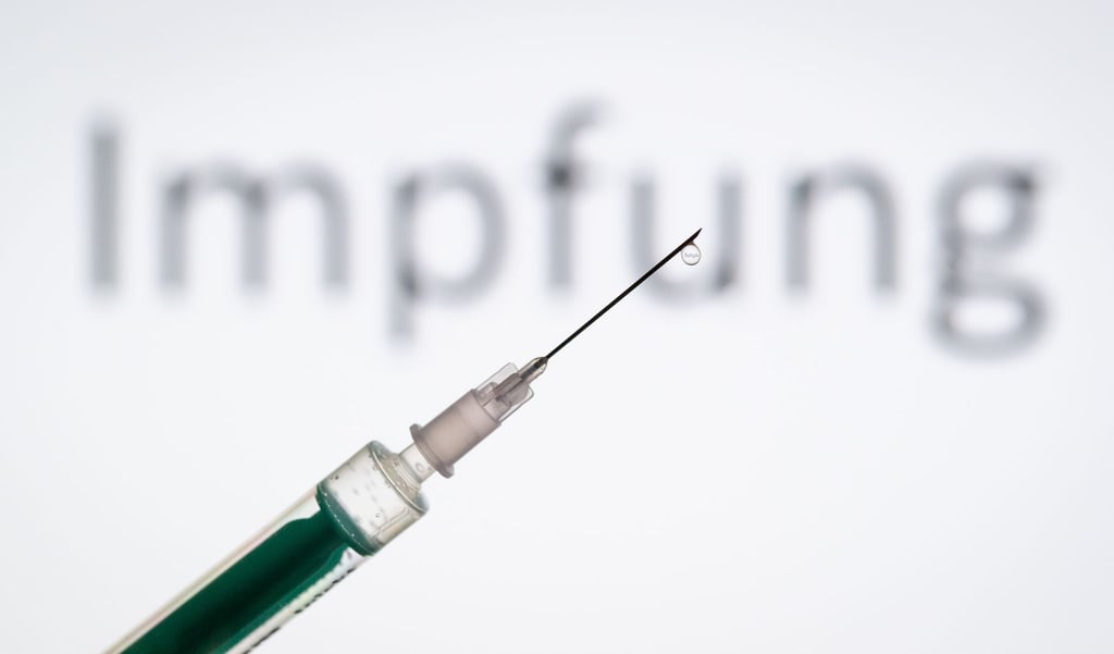 Eine Spritze wird vor den Schriftzug „Impfung“ gehalten.