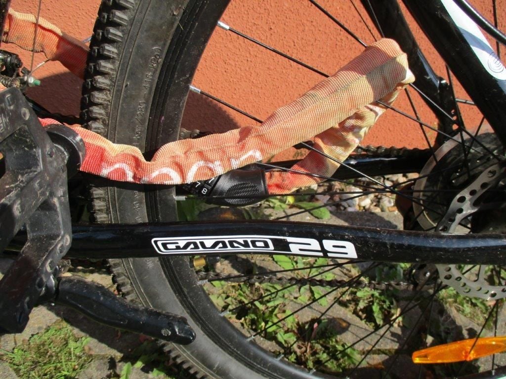 Das Fahrrad ist mit einem orangefarbenen Fahrradschloss mit Zahlenkombination gesichert.