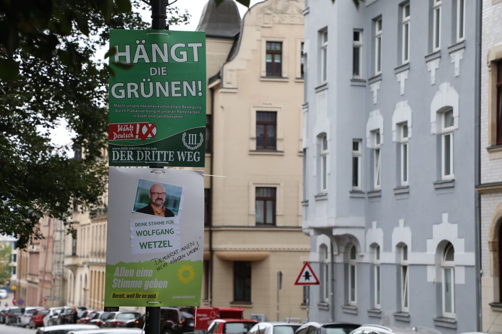 Ein umstrittenes Wahlplakat der Splitterpartei „III Weg“ hängt über einem Plakat der Grünen.