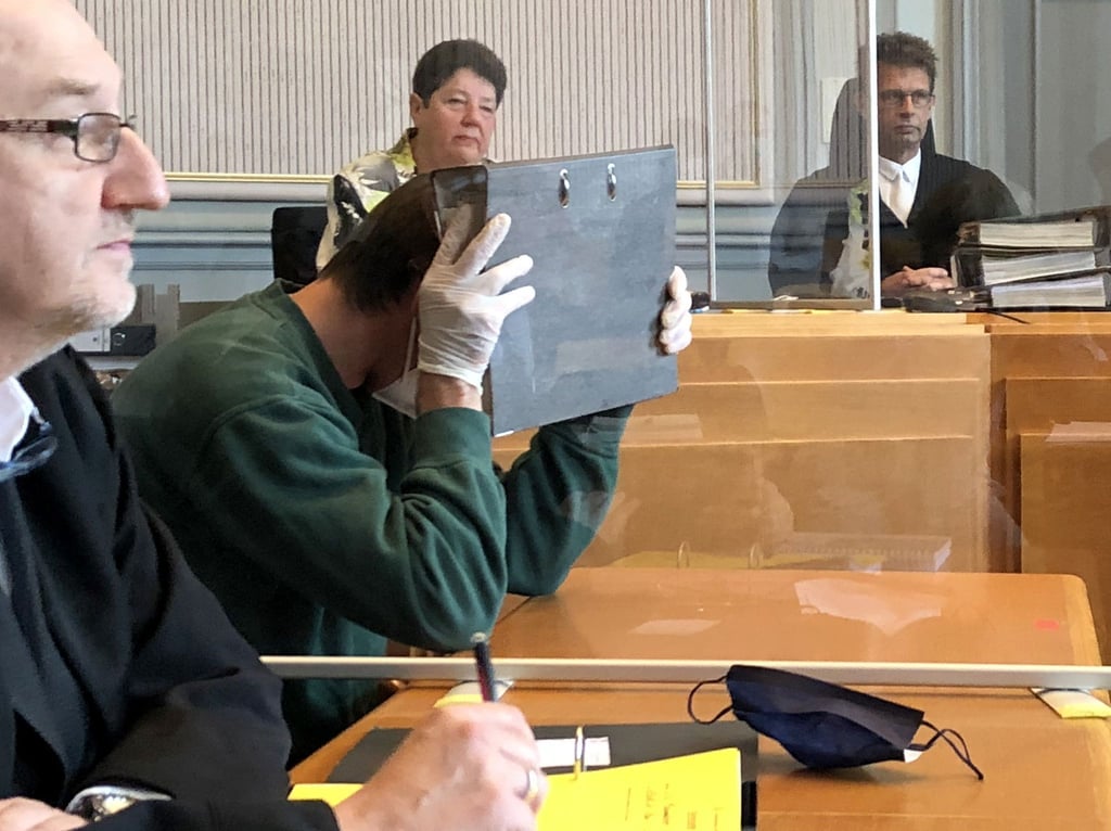 Der Angeklagte versteckt sein Gesicht im Gericht hinter einem Aktenordner.