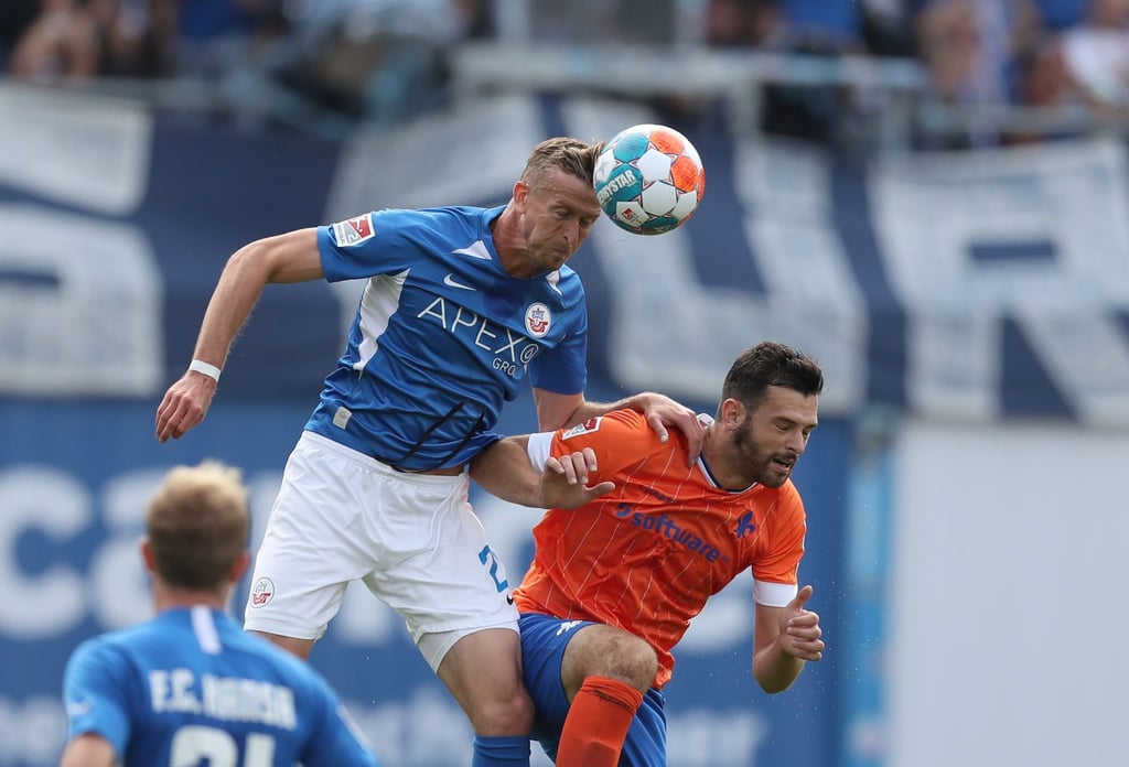 Rostocks Thomas Meißner (l) klärt vor Darmstadts Luca Pfeiffer (r) per Kopf den Ball aus der Gefahrenzone.
