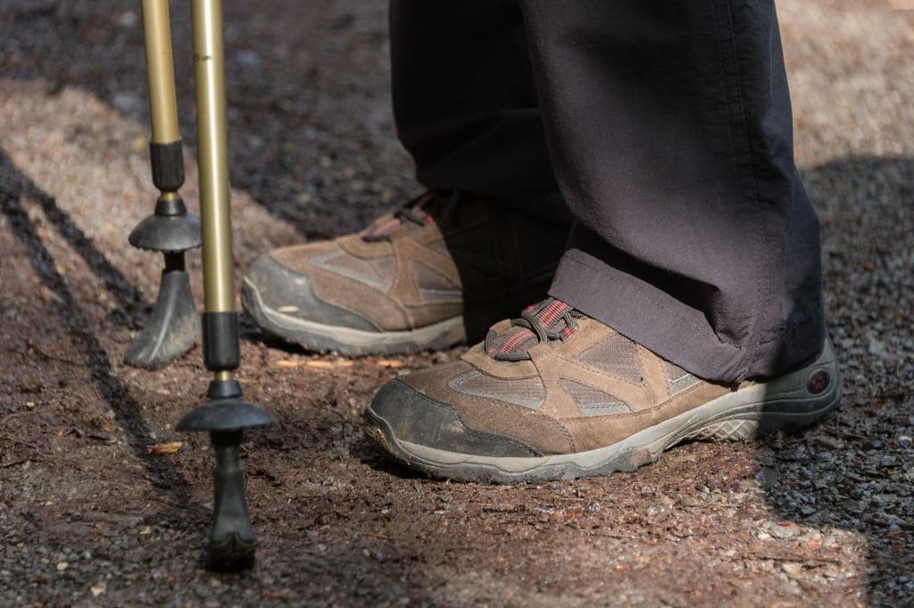 Eine Teilnehmerin mit Wanderschuhen und Trekkingstöcken wartet auf den Beginn ihrer Wanderung.