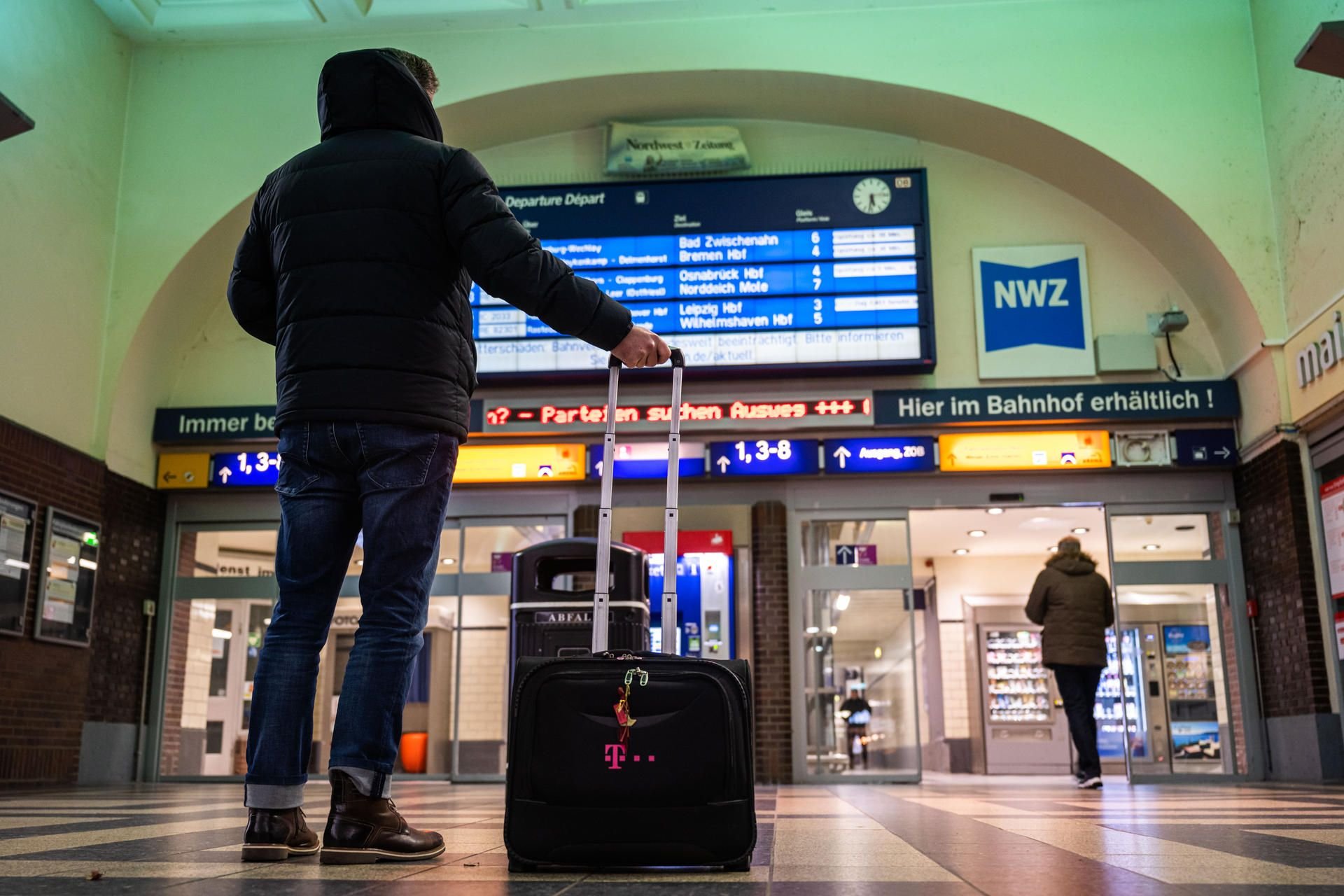 Ein Reisender steht am frühen Morgen in einem Hauptbahnhof und informiert sich an der Anzeigetafel der Deutschen Bahn.