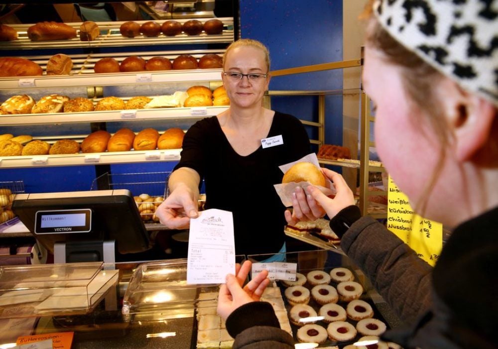 Peggy Simroth, Verkäuferin bei der Bäckerei Latsch, übergibt einer Kundin ein Brötchen und einen Kassenbon.
