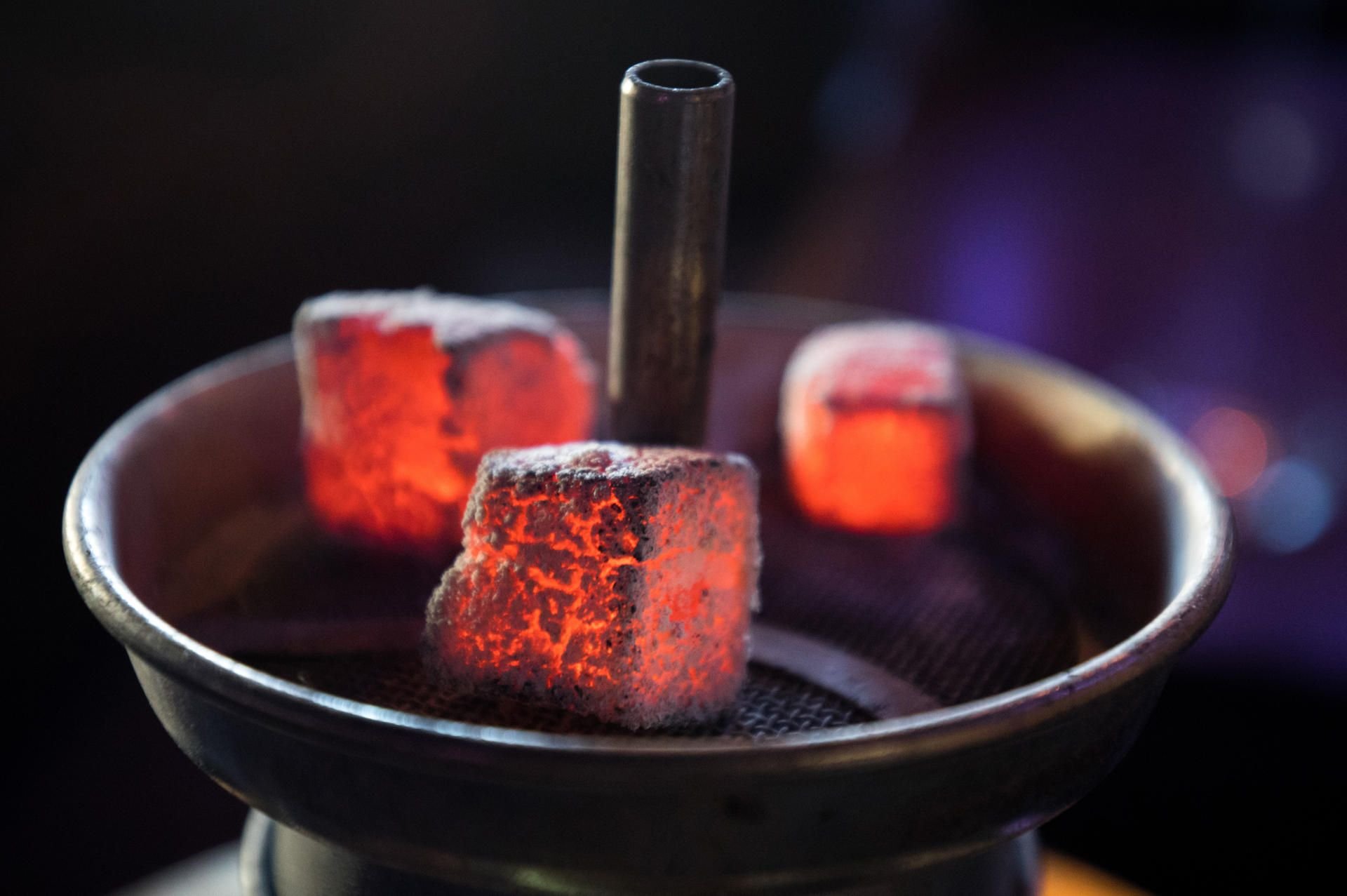 Glühende Kohle liegt auf einem Metallsieb über dem Tabak im Kopf einer Wasserpfeife in einer Shisha-Bar.