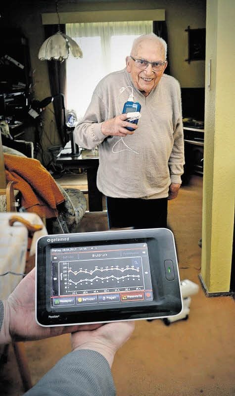 Harri Schmidt zeichnet mit dem kleinen Gerät, das er in der Hand hält, täglich ein EKG auf. Dazu muss er nichts weiter machen, als sich das Gerät auf die Brust zu legen. Die Werte werden dann über eine Sendestation (vorn) per Mobilfunk nach Berlin gesendet.