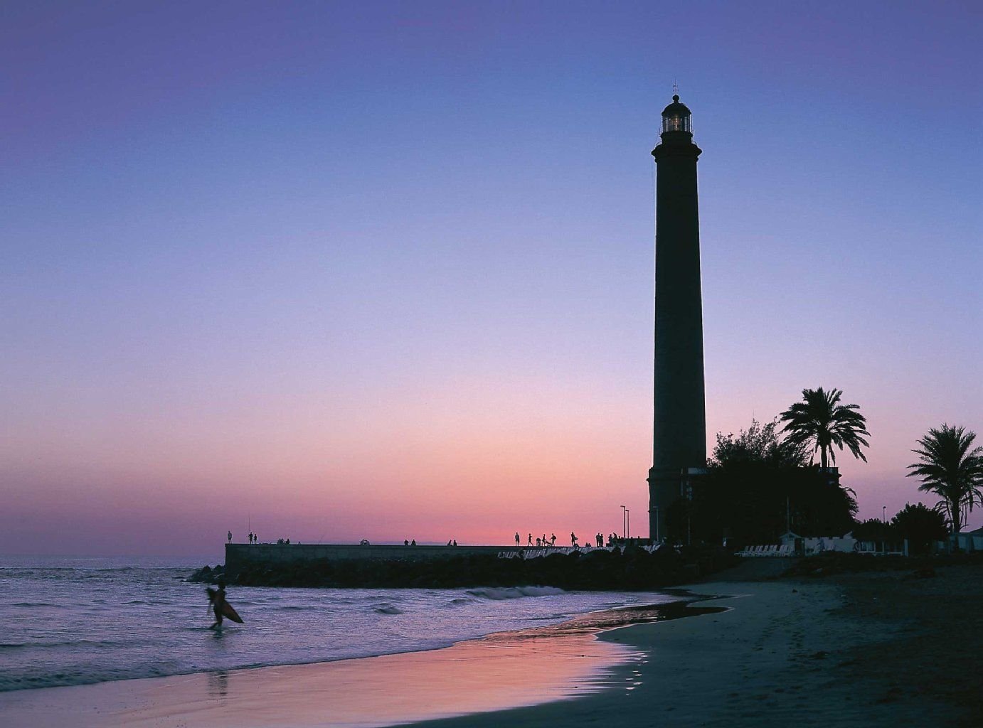 Der Leuchtturm an der Promenade von Maspalomas auf Gran Canaria zeichnet sich dunkel vor dem Abendhimmel ab.