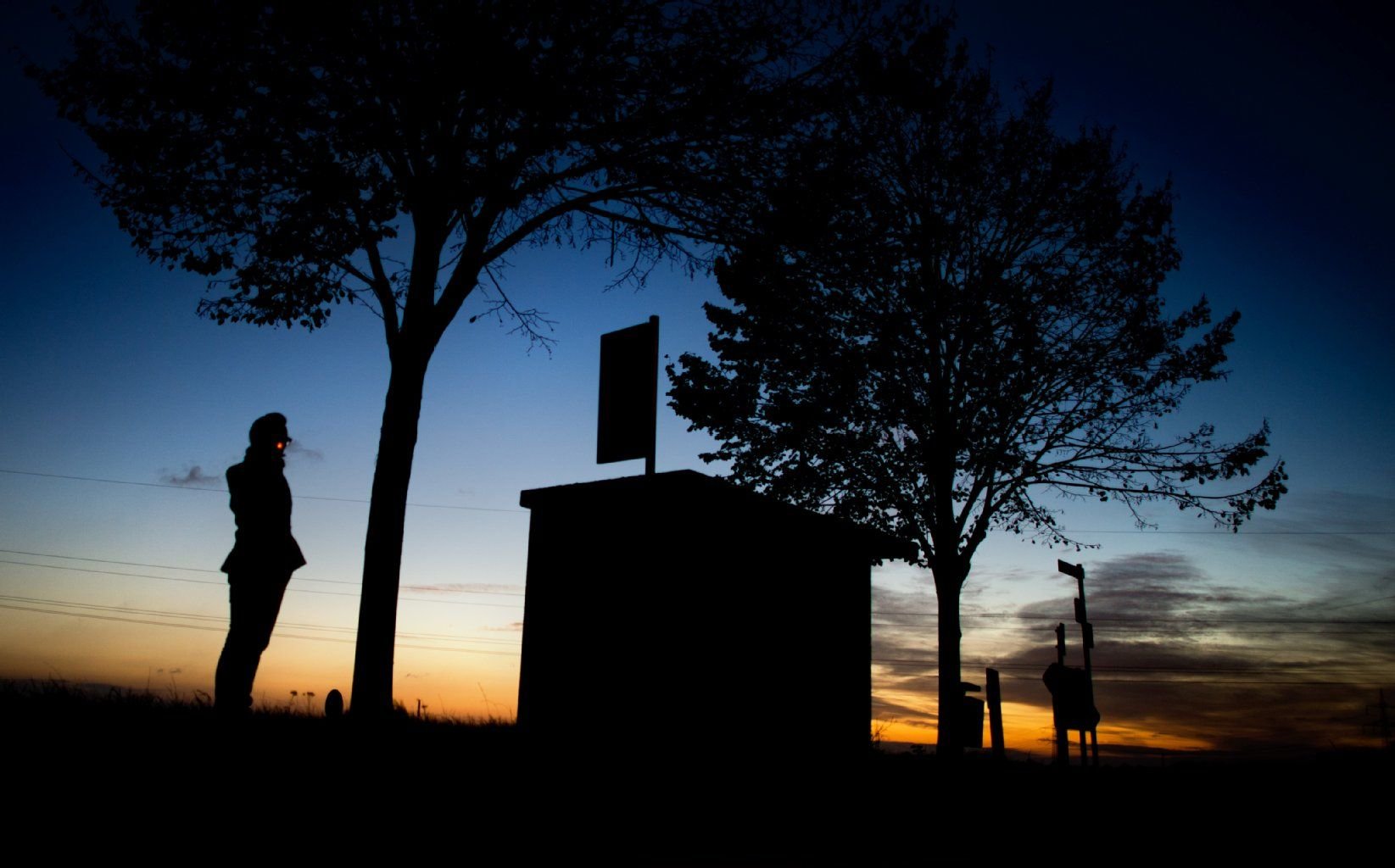 Ein junger Mann wartet kurz vor Sonnenaufgang auf seinen Bus an einer Bushaltestelle an einer Landstraße.