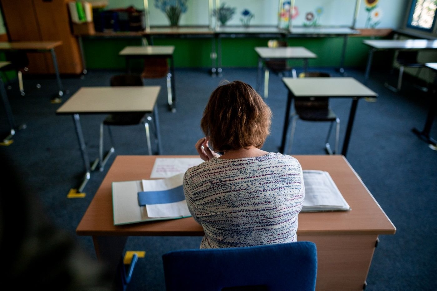 Eine Lehrerin sitzt an einem Pult im Klassenraum. An vielen schulen wird sich intensiv auf den Schulbeginn vorbereitet.