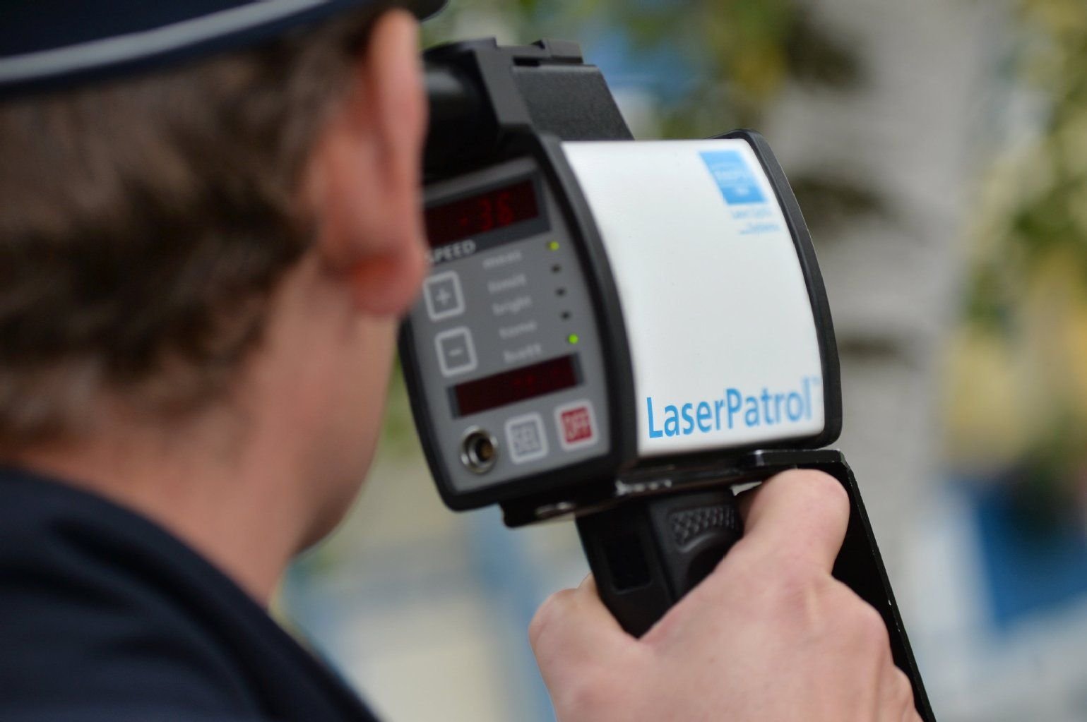Ein Polizeibeamter misst mit einem Handlasergerät die Geschwindigkeit eines vorbeifahrenden Autos.