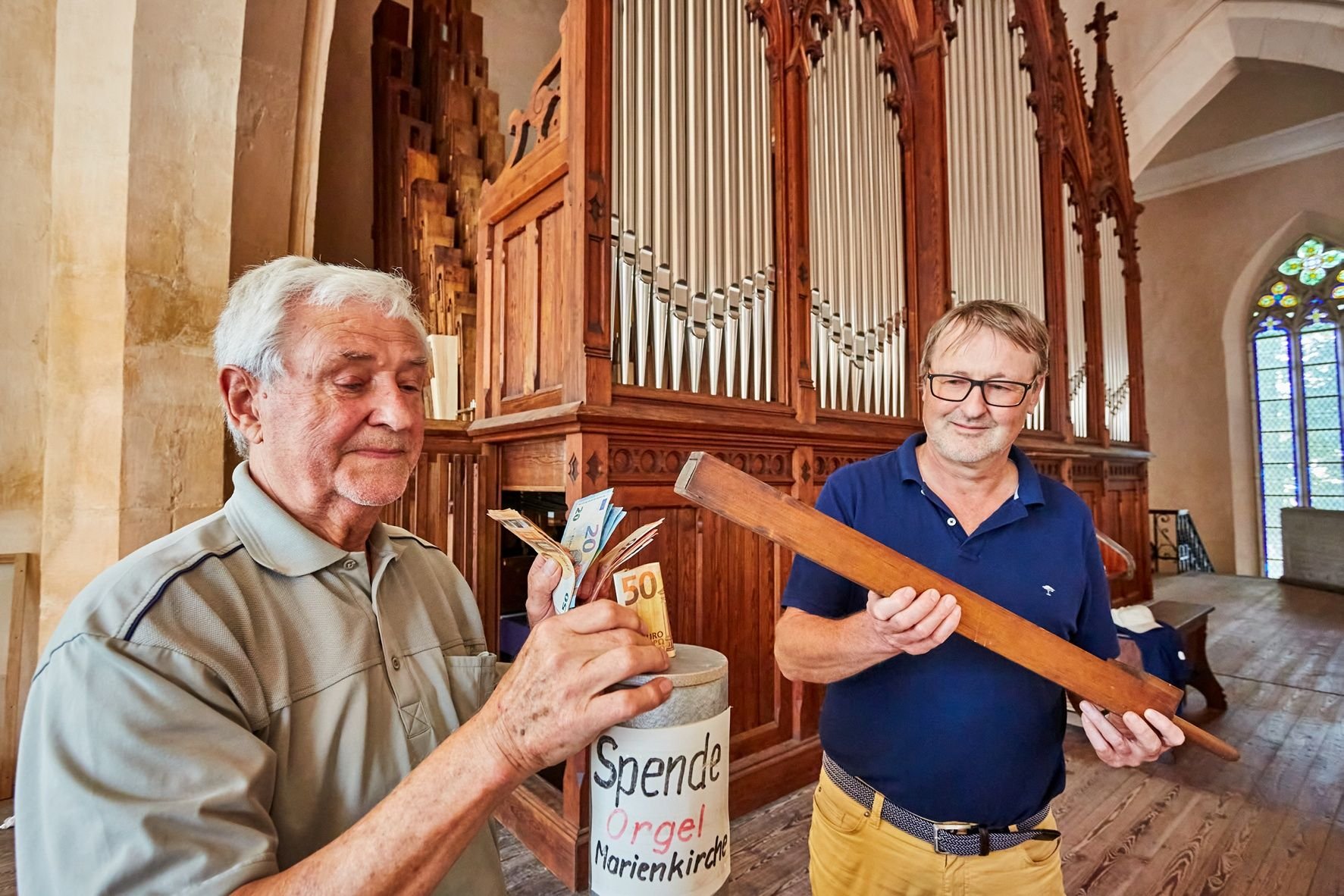 Dieter Wöhlbier (li.) steckt das Geld für die Orgel in seine selbst gebaute Orgelpfeife. Pfarrer Johannes Lewek überreicht ihm als Dankeschön eine alte Orgelpfeife.