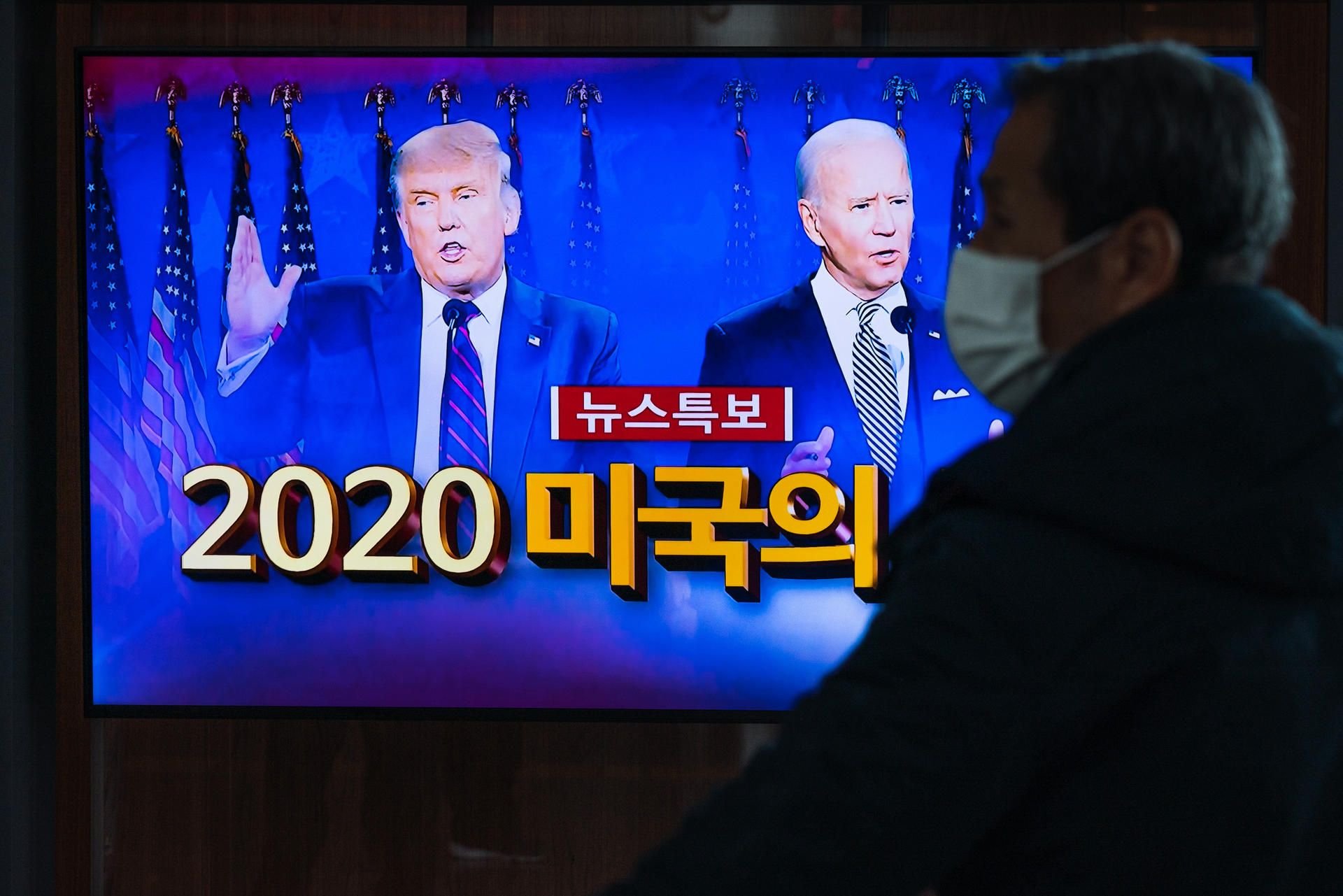 Ein Mann mit einer Mund-Nasen-Bedeckung verfolgt am Bahnhof von Seoul eine Nachrichtensendung über die Präsidentschaftswahlen in den USA.