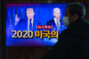 Ein Mann mit einer Mund-Nasen-Bedeckung verfolgt am Bahnhof von Seoul eine Nachrichtensendung über die Präsidentschaftswahlen in den USA.