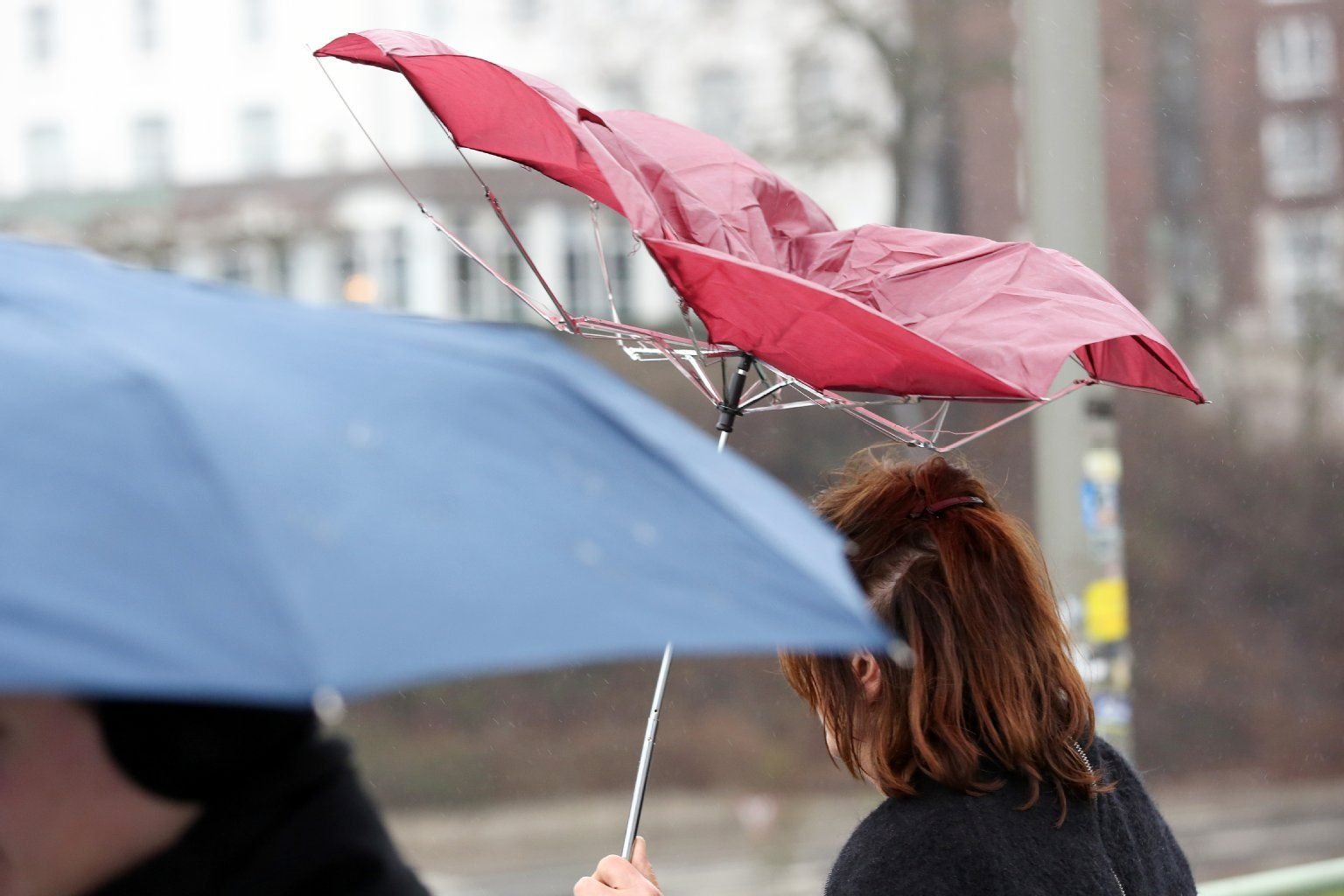 Passanten schützen sich mit Regenstürmen gegen Regen und Sturm.