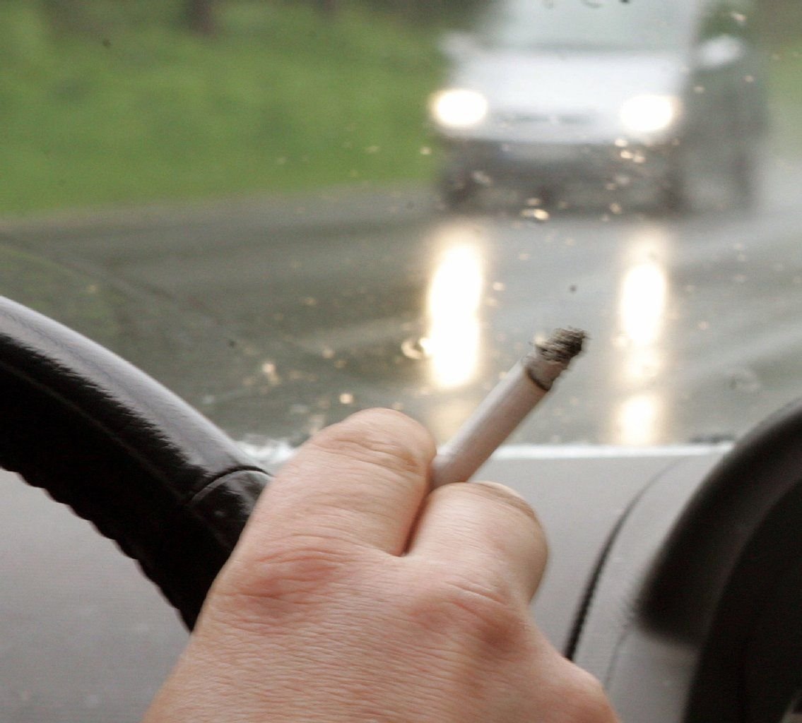 Ein Autofahrer raucht am Steuer seines Fahrzeugs.
