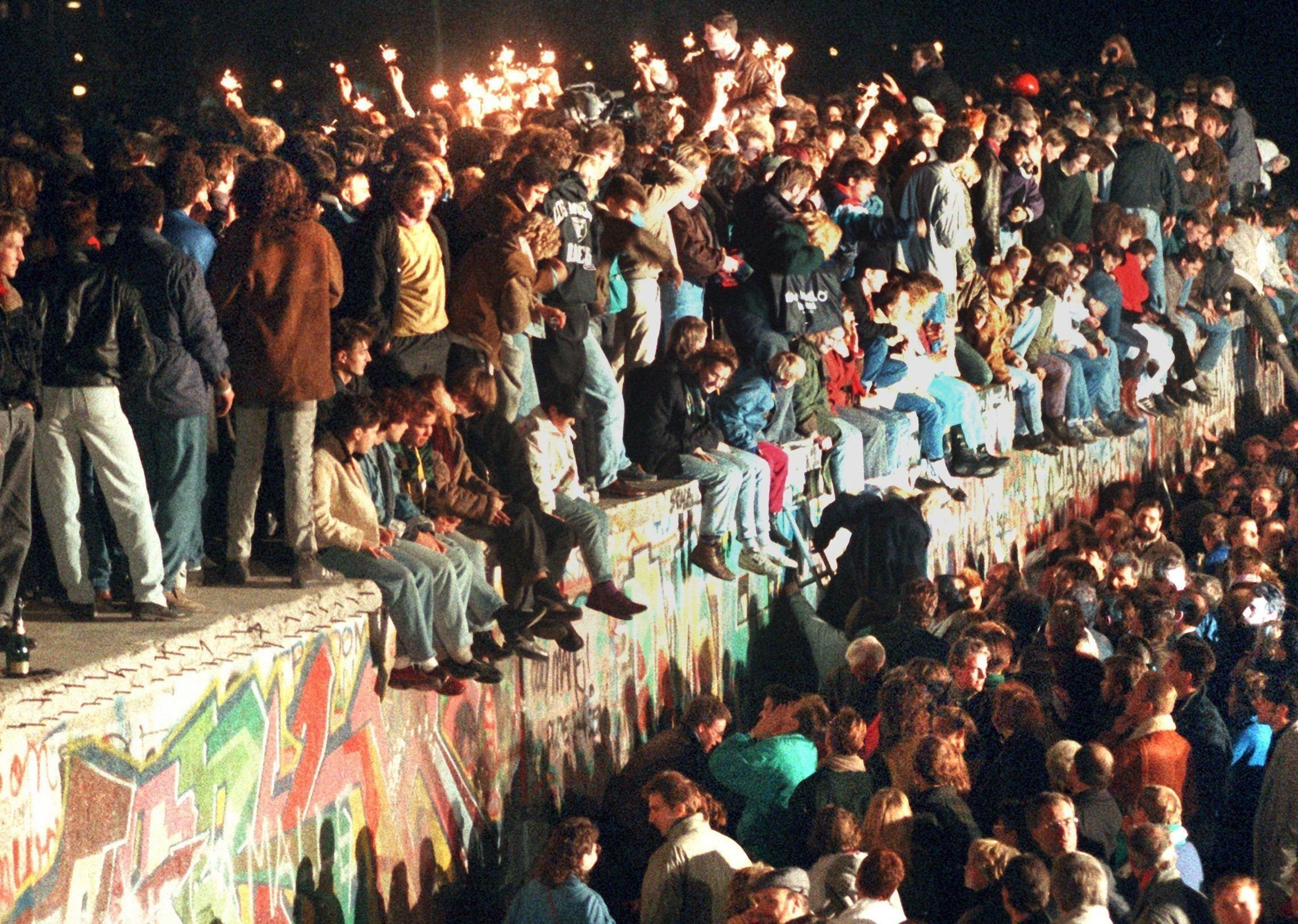 Jubelnde Menschen sitzen mit Wunderkerzen auf der Berliner Mauer