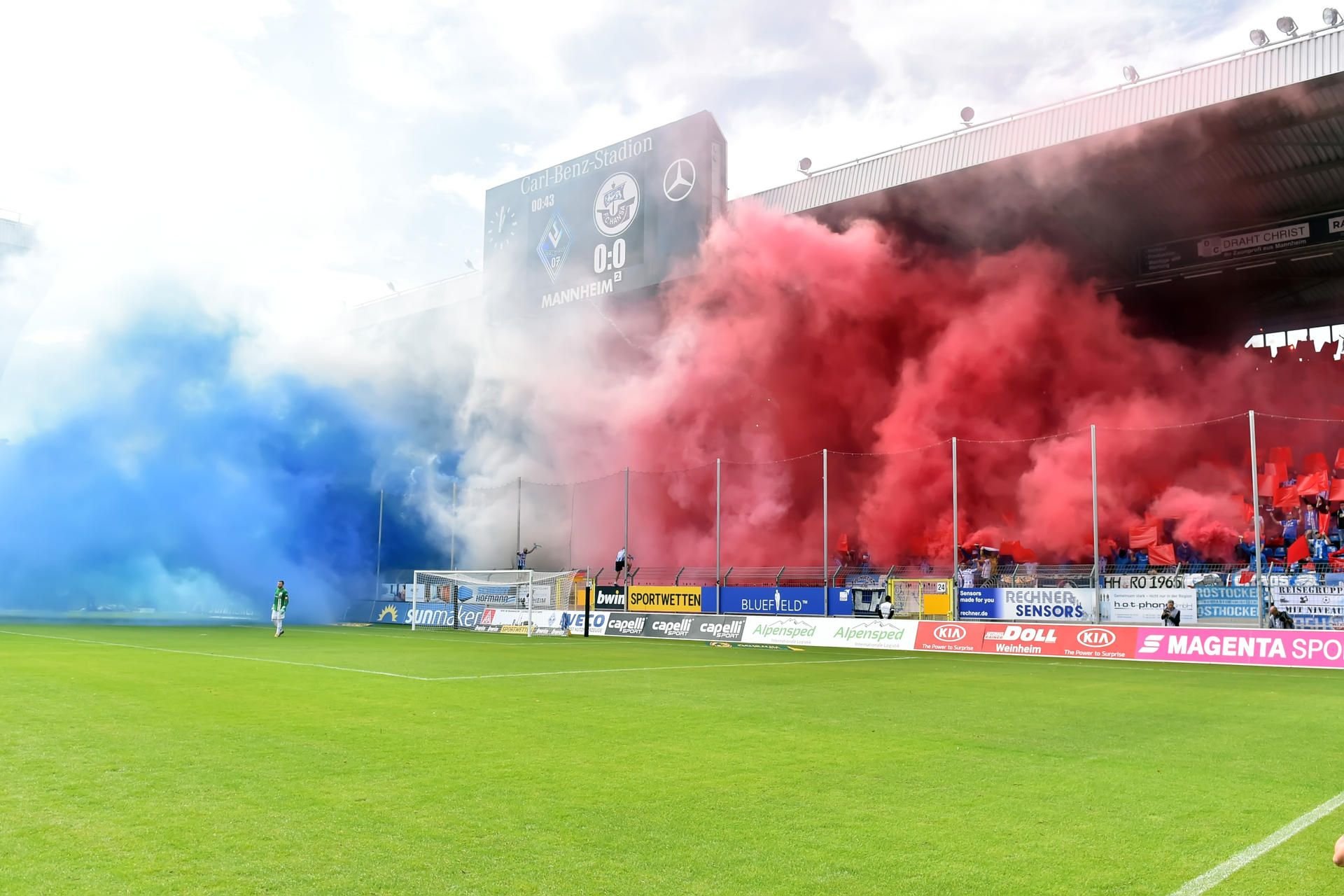 Rauch in den Vereinsfarben weht aus dem Hansa-Fanblock in Mannheim auf das Spielfeld.