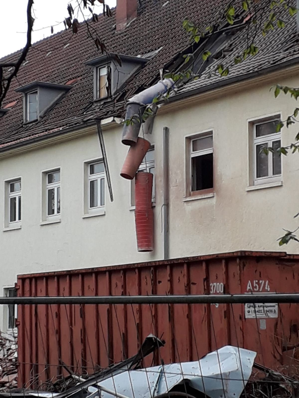 Die zerbrochenen Platten eines rötlich-weißen Materials wurden über eine Schuttrutsche in einen Container entsorgt, die Elemente der Schuttrutsche waren nicht verbunden.