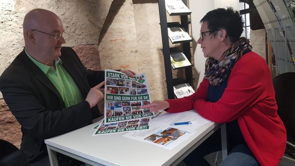 Uwe Schmidt, Leiter der Stadtinformation in Harzgerode, und Mitarbeiterin Uta Zacharias mit einem der „Kaufen Sie vor Ort“-Plakate.